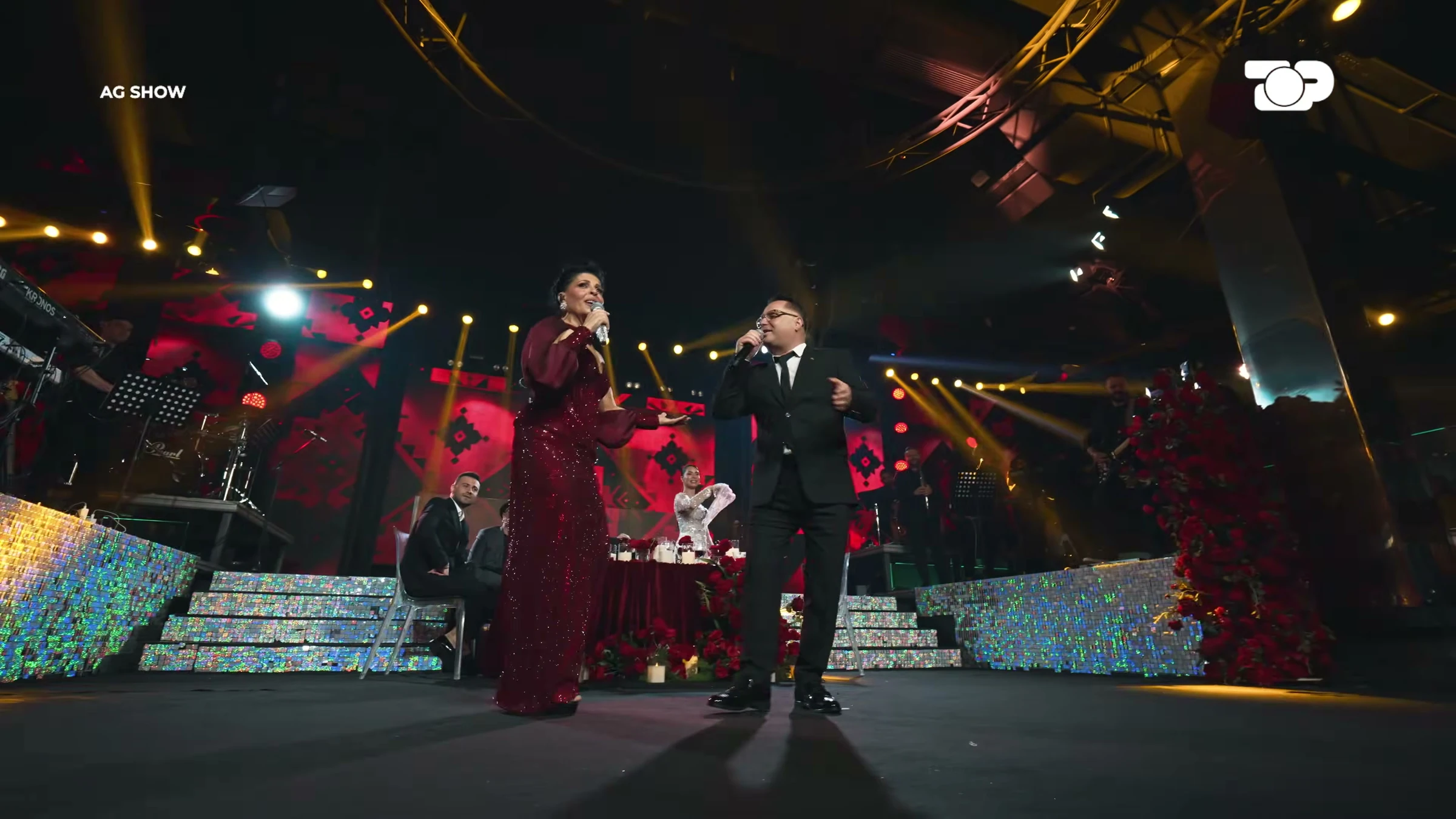 AG Show — Wide real set, singers and warm lighting; preserves programme watermarks.