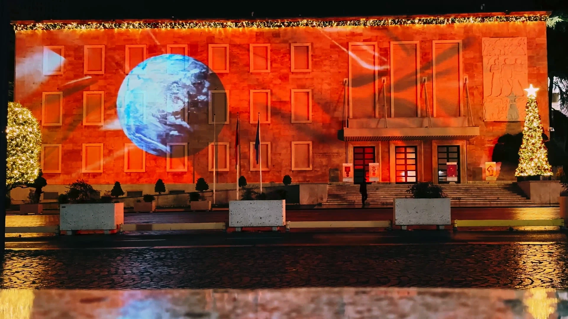 Prime Minister’s Office — JKN tribute 2024 — Blue globe against red façade and wet-street reflections